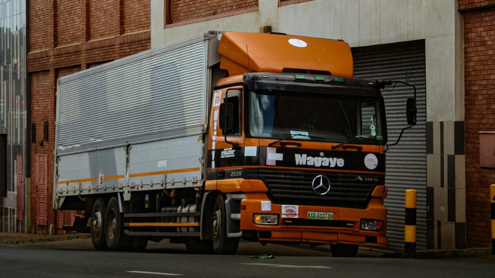 A large orange truck parked beside a brick industrial building in Mbabane, Eswatini.