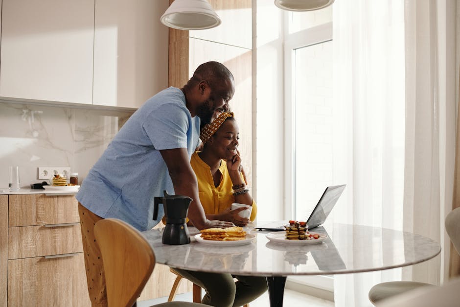 A joyful couple sharing breakfast and working on a laptop in their cozy kitchen.